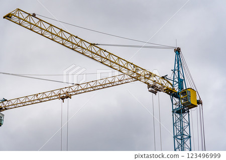 Tall construction cranes reach for the sky, their yellow and blue structures stark against the overcast backdrop, highlighting a city in development Tall construction cranes reach for the sky, their yellow and blue structures stark against the overcast backdrop, highlighting a city in development 123496999