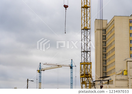 Several construction cranes are busy lifting materials at a house construction site located in a bustling urban environment during overcast weather 123497033