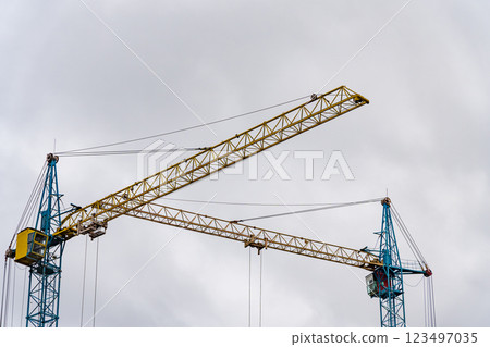 Two towering construction cranes are actively engaged in the building process of a new house, surrounded by a cloudy sky in the early morning Two towering construction cranes are actively engaged in the building process of a new house, surrounded by a cloudy sky in the early morning 123497035