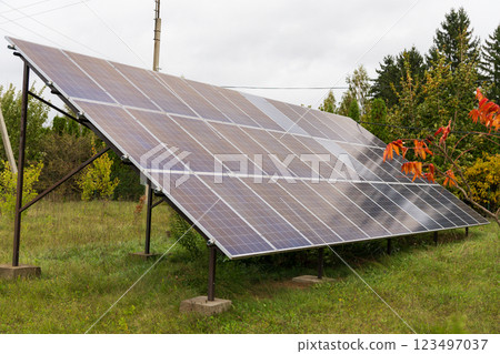 Solar panels are strategically positioned on a metal frame, capturing sunlight in a green field while surrounded by trees and foliage on a cloudy day Solar panels are strategically positioned on a metal frame, capturing sunlight in a green field while surrounded by trees and foliage on a cloudy day 123497037