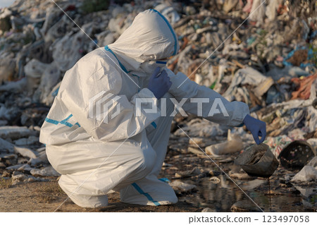 A dedicated environmental scientist, clad in protective gear, kneels by a polluted water body to gather samples amid a backdrop of waste and debris, highlighting environmental concerns A dedicated environmental scientist, clad in protective gear, kneels by a polluted water body to gather samples amid a backdrop of waste and debris, highlighting environmental concerns 123497058