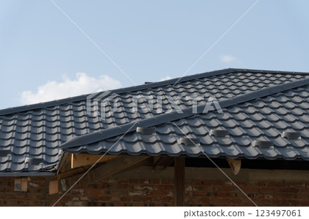 A skilled worker meticulously installs a black tiled roof atop a newly constructed home 123497061