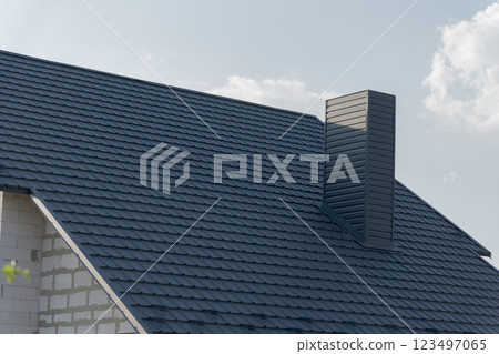 A beautiful modern house boasts a stylish dark slate roof, highlighting the clean lines and architectural design. Sunlight reflects off the roof shingles as clouds drift lazily A beautiful modern house boasts a stylish dark slate roof, highlighting the clean lines and architectural design. Sunlight reflects off the roof shingles as clouds drift lazily 123497065