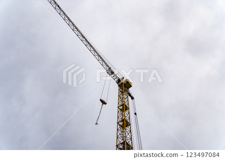 A tall construction crane looms over the skyline, its yellow structure contrasting with the grey clouds. It is actively involved in lifting materials for a new building project A tall construction crane looms over the skyline, its yellow structure contrasting with the grey clouds. It is actively involved in lifting materials for a new building project 123497084