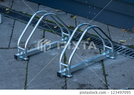 Two sleek metal bicycle racks stand on a paved surface, ready to provide secure parking for bicycles. The sleek design adds a modern touch to the urban environment 123497095