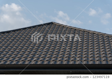 Under a pristine blue sky, a contemporary roof glistens in the sunlight, highlighting its sleek design and intricate tile pattern, evoking a sense of tranquility and harmony with nature 123497119