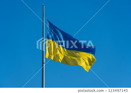 A blue and yellow Ukrainian flag is hoisted on a tall pole, fluttering gently in the wind. The bright colors contrast beautifully against the clear, azure sky A blue and yellow Ukrainian flag is hoisted on a tall pole, fluttering gently in the wind. The bright colors contrast beautifully against the clear, azure sky 123497145