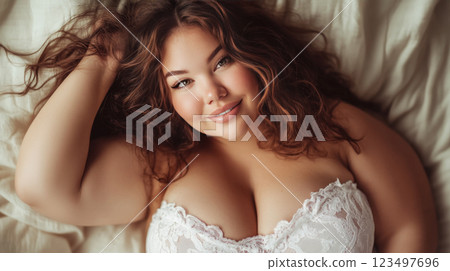 Plus-size woman in lacy underwear lying on bed, embracing her beauty. 123497696
