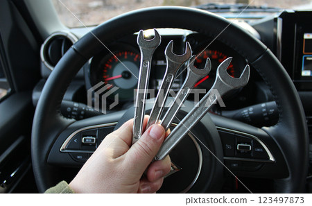 A mechanic holds a bunch of variety diameter wrenches in front of the steering wheel and blurred dashboard in car with the ignition on A mechanic holds a bunch of variety diameter wrenches in front of the steering wheel and blurred dashboard in car with the ignition on 123497873