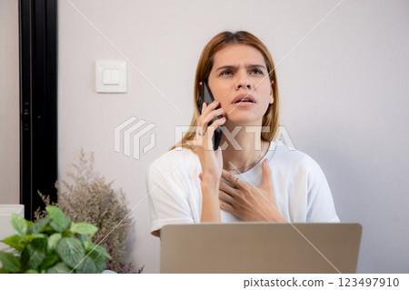 Young caucasian businesswoman working on laptop computer while talking on smartphone with stress. 123497910