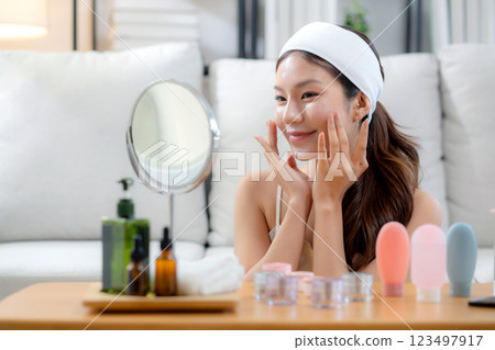 Beauty young asian woman applying cream on facial for wrinkles while looking mirror in living room. 123497917