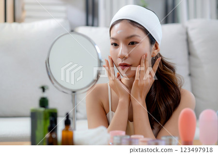 Beauty young asian woman applying cream on facial for wrinkles while looking mirror in living room. Beauty young asian woman applying cream on facial for wrinkles while looking mirror in living room. 123497918