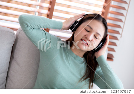 Happy young asian woman wearing headphones listening music while sitting on sofa with fun. Happy young asian woman wearing headphones listening music while sitting on sofa with fun. 123497957