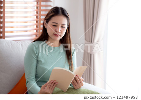 Young asian woman reading a book with expression sitting on sofa in living room at home. Young asian woman reading a book with expression sitting on sofa in living room at home. 123497958
