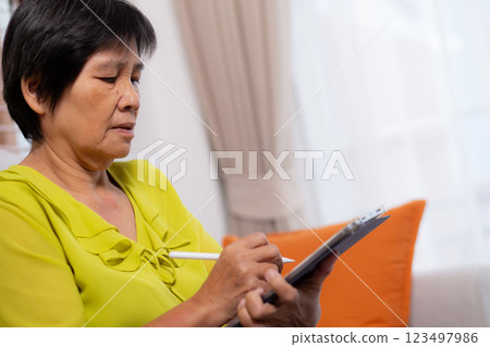 Senior asian woman sitting on sofa using digital tablet with relax in living room at home. 123497986