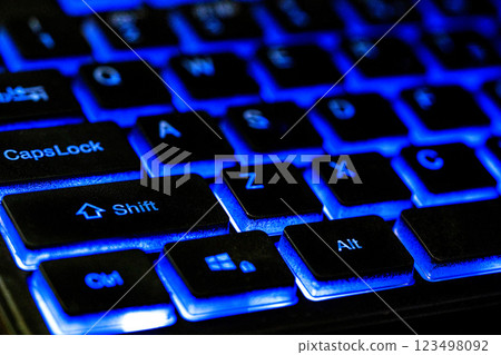 Close-up of a backlit keyboard showcasing illuminated keys in vibrant blue, highlighting the Shift, CapsLock, and Alt keys against a dark background. 123498092