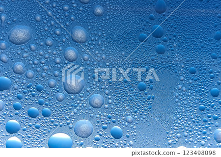 Water droplets cluster on a blue surface, creating a captivating abstract pattern that highlights the beauty of nature and moisture. 123498098