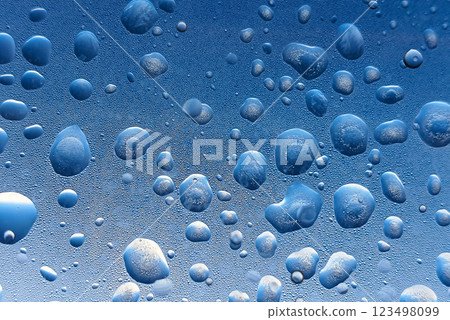 Mesmerizing droplets of water glisten against a blue backdrop, creating a serene and refreshing atmosphere, evoking a sense of tranquility and clarity. 123498099