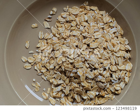 A close-up view of a mound of rolled oats on a beige plate, showcasing their golden color and texture, perfect for a healthy meal. 123498119