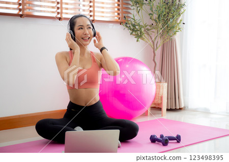 Young asian woman watch laptop after practice yoga and workout and listening music on headphone. 123498395