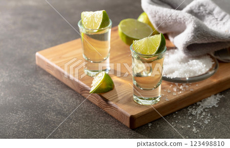 Tequila with sea salt and lime slices on a cutting board. Tequila with sea salt and lime slices on a cutting board. 123498810