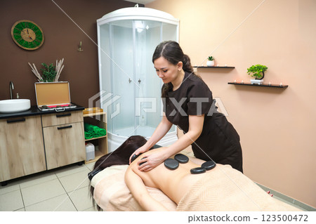 Massage Therapist Placing Hot Stones on Client's Back and Lower Back for Relaxation Therapy. General plan 123500472