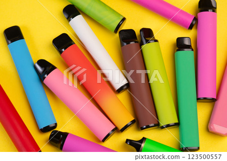 Layout of colorful disposable electronic cigarettes on a yellow background. The concept of modern smoking 123500557