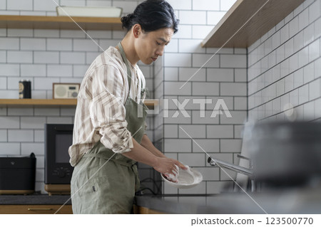 A man in his 40s washing dishes in the kitchen, profile 123500770