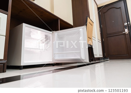 mini fridge in low angle view, inside it empty shelves placed under wooden counter and next to wood closet and chair in a luxury hotel room. 123501193
