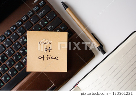 Sticky note with handwritten phrase out of office on a laptop with pen and notebook top view Sticky note with handwritten phrase out of office on a laptop with pen and notebook top view 123501221