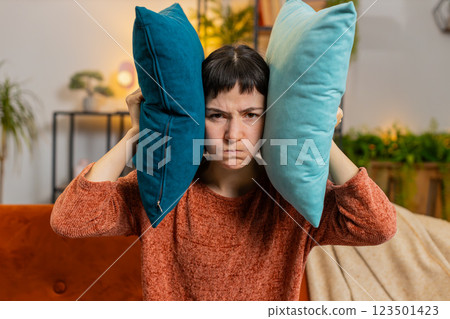 Irritated woman girl covers ears with cushions, annoyed by noisy neighbors suffers from headache Irritated woman girl covers ears with cushions, annoyed by noisy neighbors suffers from headache 123501423