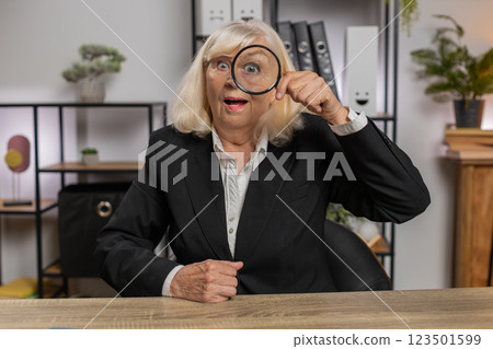 Smiling senior businesswoman looking through magnifying glass with wow expression at home office 123501599