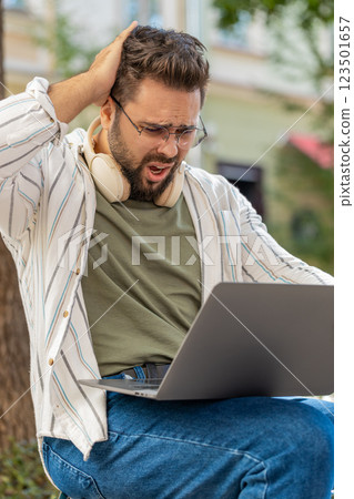 Caucasian young man using laptop browsing loses lottery results, bad news sitting in city street Caucasian young man using laptop browsing loses lottery results, bad news sitting in city street 123501657