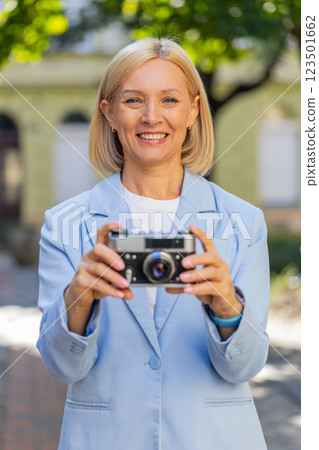 Happy mature businesswoman using vintage camera to take photos of fascinating city on street 123501662