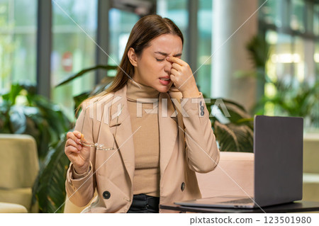 Overworked businesswoman suffering from eye strain and headache working on laptop in office lobby 123501980