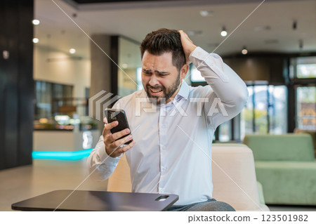 Young businessman using mobile phone becomes shocked sudden lottery results in office hotel lobby 123501982