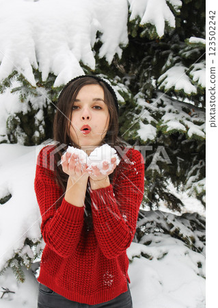 Girl in red christmas sweater playing with the snow outside near the tree in snow Girl in red christmas sweater playing with the snow outside near the tree in snow 123502242