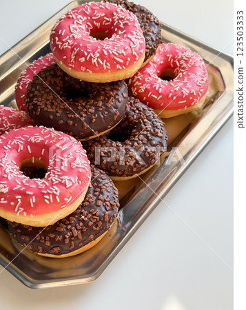 Many pink and brown donuts on metal tray close up Many pink and brown donuts on metal tray close up 123503333