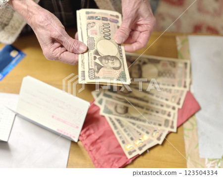 一位老婦人一邊數著新版一萬日元鈔票,一邊把存摺放在 一位老婦人一邊數著新版一萬日元鈔票,一邊把存摺放在 123504334
