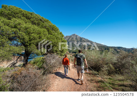 Caucasian male and female hiking in scenic mountain trail under clear blue sky 123504578