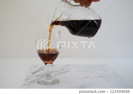 Pouring cola from a jug into a glass on a white background 123504686