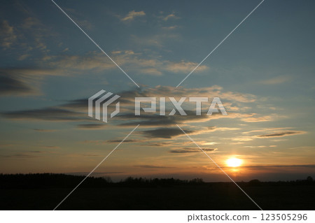 The setting sun through the clouds over the field in the silence of the evening 123505296