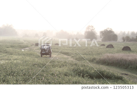 Jeep Driving Through Misty Field with Hay Bales 123505313