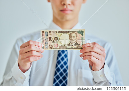 一名二十多歲的年輕人手裡拿著一張一萬日元的鈔票 一名二十多歲的年輕人手裡拿著一張一萬日元的鈔票 123506135