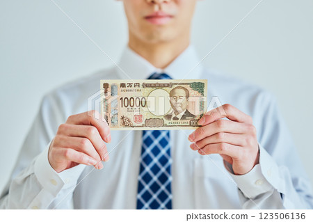 一名二十多歲的年輕人手裡拿著一張一萬日元的鈔票 一名二十多歲的年輕人手裡拿著一張一萬日元的鈔票 123506136