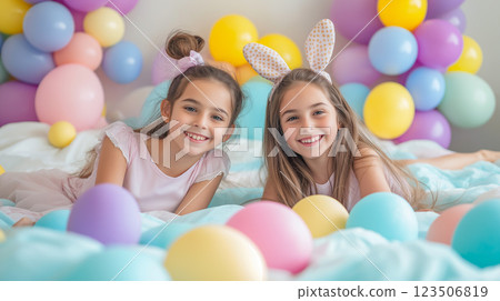 Two girls enjoy a festive celebration with pastel balloons and colorful eggs in a bright setting 123506819
