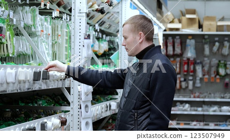 Focused electrician choosing electrical materials in hardware store for wiring, construction, and repair. A man in a hardware store, choosing sockets and switches. Focused electrician choosing electrical materials in hardware store for wiring, construction, and repair. A man in a hardware store, choosing sockets and switches. 123507949