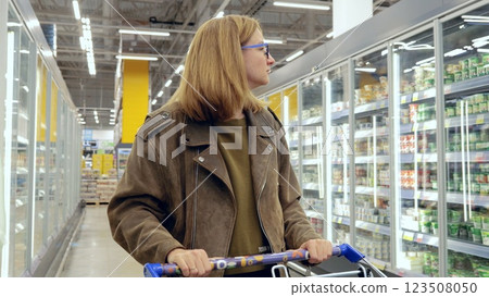 Young woman browsing dairy products in the refrigerated section of a supermarket, pushing a shopping cart Young woman browsing dairy products in the refrigerated section of a supermarket, pushing a shopping cart 123508050
