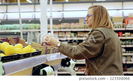 Young woman choosing lemons in a supermarket, picking up a lemon from a shelf full of fresh produce in the fruit and vegetable aisle Young woman choosing lemons in a supermarket, picking up a lemon from a shelf full of fresh produce in the fruit and vegetable aisle 123508066