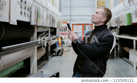 Customer browsing a smartphone app for carpet information while shopping in a home improvement store to find the perfect product. A man in a hardware store choosing flooring. Customer browsing a smartphone app for carpet information while shopping in a home improvement store to find the perfect product. A man in a hardware store choosing flooring. 123508112